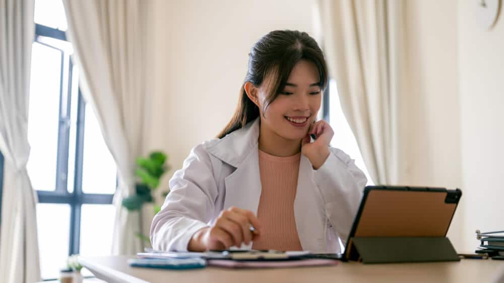 Smiling, female doctor, wearing white coat, using digital tablet for online education. Media credit: © simon2579 / Getty Images / iStock